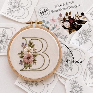 May include: A 4-inch wooden embroidery hoop containing fabric with a stitched letter B decorated with pink, white, and green floral embroidery. Surrounding the hoop are several white adhesive stick and stitch embroidery design patches.