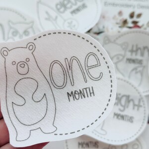 May include: White baby milestone sticker with a black outline of a bear and the text "one month".