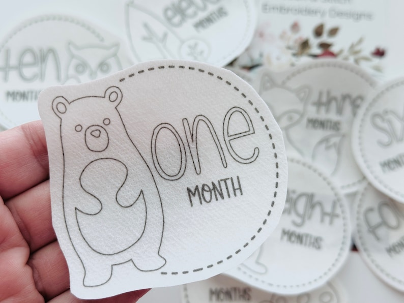 May include: White baby milestone sticker with a black outline of a bear and the text "one month".