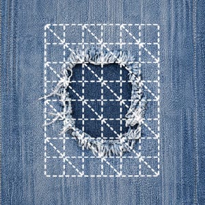 May include: Close-up of a denim fabric with a distressed area. The frayed edges of the hole are visible, with a white grid pattern overlaying the damaged section. The background is a medium blue denim.