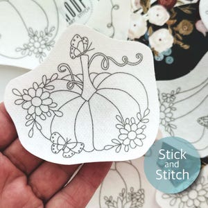 May include: A white fabric with a black line drawing of a pumpkin with butterflies and flowers. The text "Stick and Stitch" is in the lower right corner of the image.