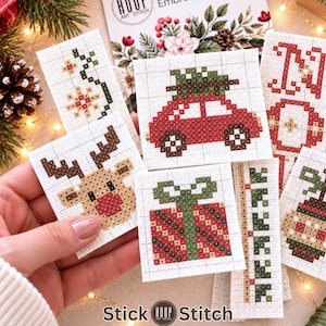 May include: A collection of small, square cross-stitch fabric pieces featuring holiday designs including a red car with a tree, a reindeer with a red nose, a gift box, and floral patterns. The fabric is white with a visible grid for stitching.