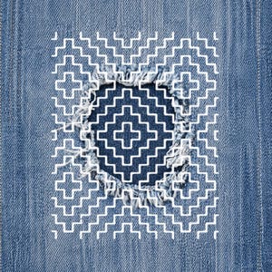May include: Close-up of a denim fabric with a distressed area repaired with white stitching. The repair features a geometric pattern of crosses and zigzags, creating a decorative patch. The denim is a medium blue color.