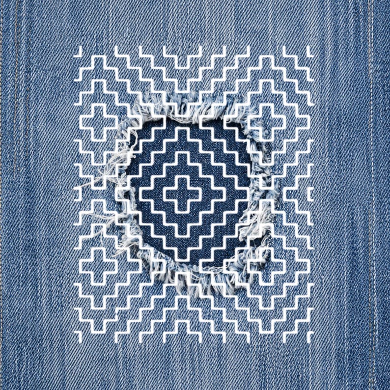 May include: Close-up of a denim fabric with a distressed area repaired with white stitching. The repair features a geometric pattern of crosses and zigzags, creating a decorative patch. The denim is a medium blue color.