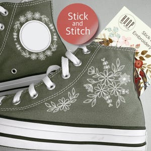 May include: Olive green high-top sneakers with white floral embroidery and white laces. The sneakers have a white rubber sole and a black stripe. A red circle with the text "Stick and Stitch" is visible.