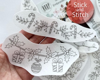 May include: A set of white fabric Christmas embroidery patterns with black outlines. The patterns include a garland with candy canes, a garland with holly and ornaments, and a garland with lights. The patterns are labeled "Stick & Stitch Embroidery Designs".
