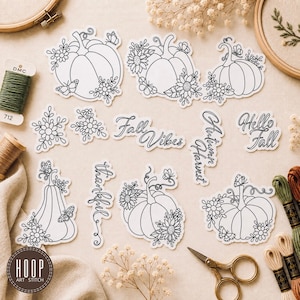 May include: A collection of black and white die-cut stickers featuring pumpkins, flowers, butterflies, and script text reading Fall Vibes, Autumn Harvest, Hello Fall, and Thankful. The stickers are arranged with embroidery supplies including thread.