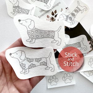 Op de afbeelding: Een set strijkbare patches met schattige teckels die truien dragen met verschillende patronen. De patches zijn op een witte achtergrond en zeggen "Stick and Stitch" in een rode cirkel.
