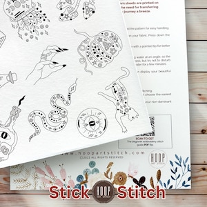 May include: A white embroidery pattern sheet featuring black line art illustrations of a hand, a pumpkin, a snake, a cat, and an eye. The sheet includes printed instructions, a QR code for a PDF guide, and the text Hoop Art Stitch at the bottom.