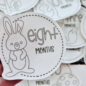 May include: White baby milestone sticker with a black outline of a bunny rabbit and the text "eight months".