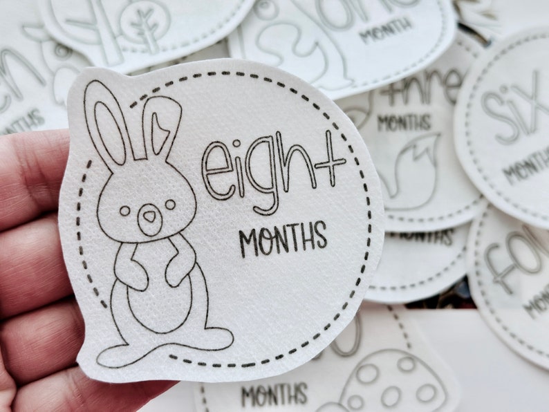 May include: White baby milestone sticker with a black outline of a bunny rabbit and the text "eight months".