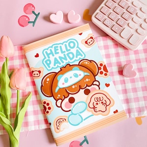 Può includere: Un quaderno blu chiaro e arancione con il testo "Hello Panda" sulla copertina. Il quaderno presenta un panda dei cartoni animati con un design di pelliccia marrone e bianca. Il quaderno è circondato da un tessuto a quadri rosa e bianco, cuori rosa e tulipani rosa.
