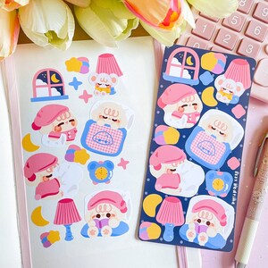 May include: A sheet of stickers featuring a cute cartoon character in various poses, including sleeping, reading, and wearing a nightcap. The stickers are on a white background and have a blue, pink, and yellow color scheme. The text "fast bedtime" is included on the sticker sheet.