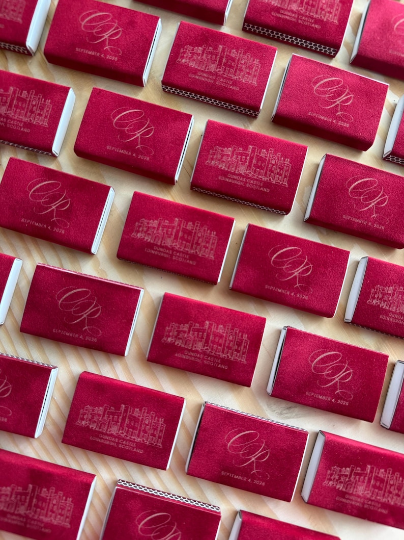 May include: A collection of rectangular matchboxes covered in deep red velvet. Some feature a gold-toned line drawing of Dundas Castle, Edinburgh, Scotland, while others display the gold-toned cursive initials CR and the date September 4, 2026.