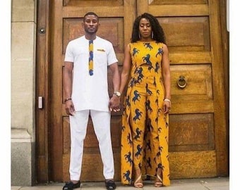 May include: A couple wearing matching white and yellow outfits with a blue and yellow patterned design. The man is wearing a white long-sleeved shirt and white trousers. The woman is wearing a yellow sleeveless top and trousers with a blue and yellow patterned design. The couple are standing in front of a wooden door.