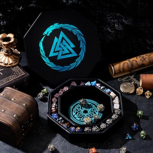 May include: A black, octagonal dice tray and box set with a blue and teal Norse design. The tray is filled with various polyhedral dice in different colors. A treasure chest and scroll are also visible.