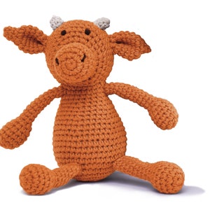 Op de afbeelding: Een gehaakt oranje knuffeldier in de vorm van een koe met witte hoorns. Het speelgoed heeft een gestikt gezicht met zwarte ogen en een bruine neus.