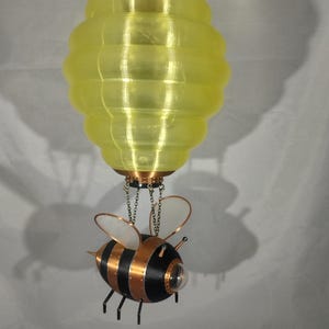 May include: A steampunk-style bee-shaped hot air balloon with a yellow, segmented balloon and black and copper body.