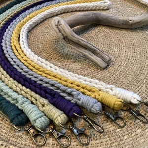 May include: A set of ten colourful braided keychains with silver key rings. The keychains are arranged in a rainbow pattern on a woven surface.