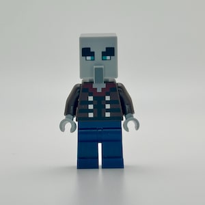 May include: A Minecraft Lego figure of a gray-faced villager with teal eyes, wearing a brown jacket over a red and white patterned shirt, and blue pants. The figure has gray hands and is standing against a white background.
