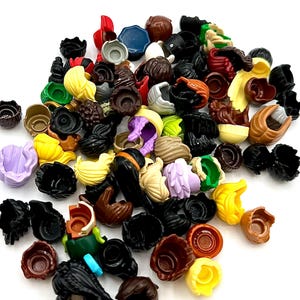May include: A collection of assorted Lego hair pieces in various colors, including black, brown, yellow, and purple. The pieces are made of plastic and are designed to fit on Lego minifigure heads. The image is taken from a top-down perspective.