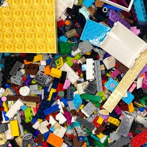 May include: A colorful assortment of plastic building blocks in various shapes and sizes. The image shows a mix of primary and secondary colors, including yellow, red, blue, green, and orange. There are also white, black, and gray blocks. The blocks are of different sizes.