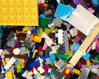 May include: A colorful assortment of plastic building blocks in various shapes and sizes. The image shows a mix of primary and secondary colors, including yellow, red, blue, green, and orange. There are also white, black, and gray blocks. The blocks are of different sizes.