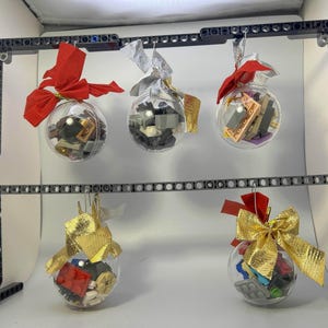 May include: Five clear glass baubles filled with colourful Lego bricks, hanging from a black metal frame. The baubles are decorated with red, gold and white ribbon.