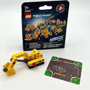 May include: A yellow LEGO Technic Mighty Machines construction vehicle toy with a movable arm, accompanied by its original cardboard packaging featuring illustrations of eight different models and a square game card with a rocky terrain graphic.