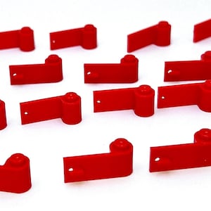 May include: A collection of bright red, rectangular plastic components, each with a cylindrical knob on one end and a small hole. The components are arranged on a white surface, suggesting a product or part for a larger item.