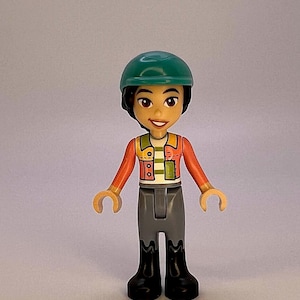 Liann wearing a coral jacket, sand blue trousers, black boots, and a dark turquoise horse riding helmet LEGO® Friends Minifigure.