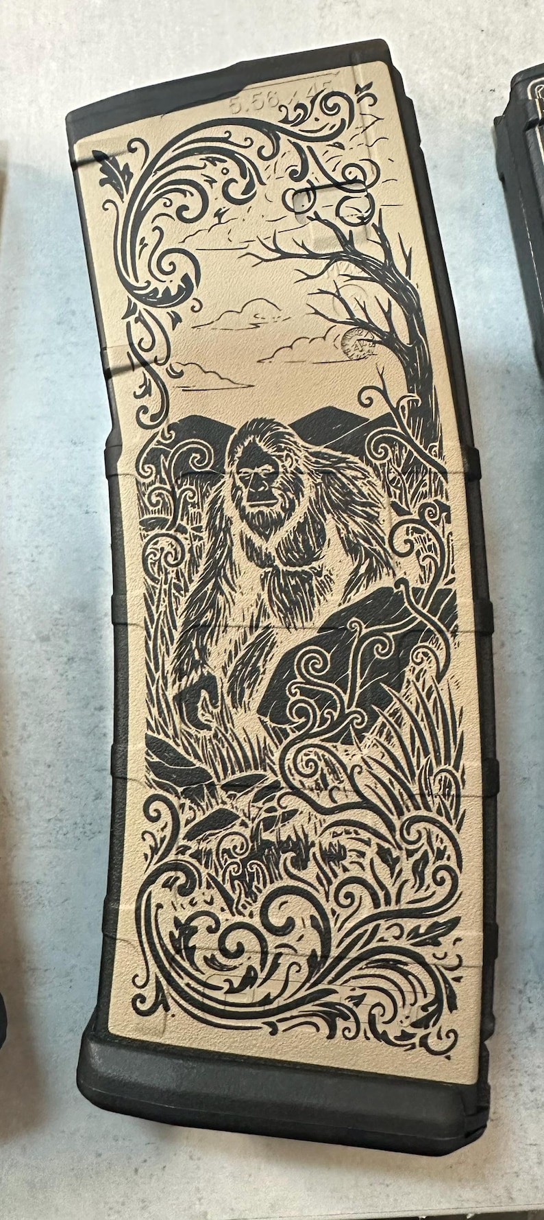 May include: Tan and black magazine with a detailed illustration of a Bigfoot in a forest scene. The design includes mountains, trees, and decorative scrollwork. The text "5.56 223" is visible.