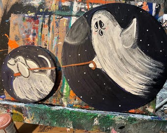 Può includere: Due decorazioni rotonde dipinte per Halloween. Una presenta un fantasma bianco con un guinzaglio, l'altra una creatura bianca simile a un cane. Entrambe sono ambientate su uno sfondo blu scuro con stelle bianche. Il fantasma tiene il guinzaglio.
