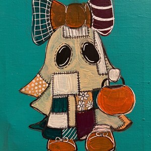 Pu&ograve; includere: Un dipinto su sfondo verde acqua raffigurante un personaggio fantasma composto da vari quadrati di tessuto patchwork nei toni del crema, bianco, verde scuro e viola. Il fantasma indossa un grande fiocco, porta un secchiello a zucca e scarpe arancioni.