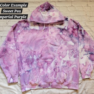 May include: A purple and white tie-dye hoodie with a hood. The hoodie has a large pocket on the front. The text "2 Color Example Sweet Pea Imperial Purple" is written on the top of the image.