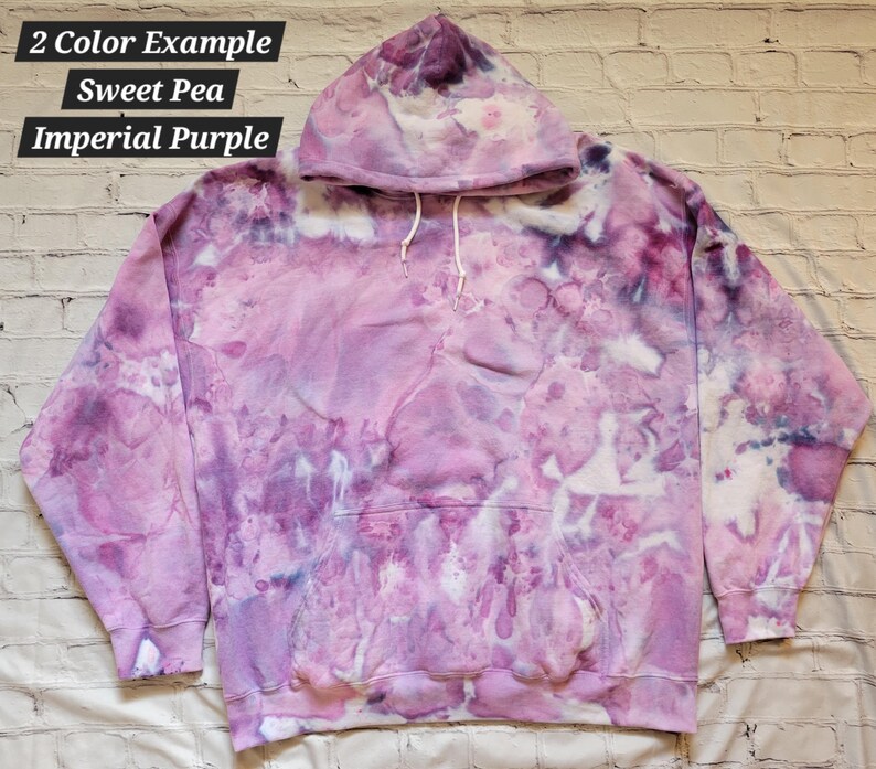 May include: A purple and white tie-dye hoodie with a hood. The hoodie has a large pocket on the front. The text "2 Color Example Sweet Pea Imperial Purple" is written on the top of the image.