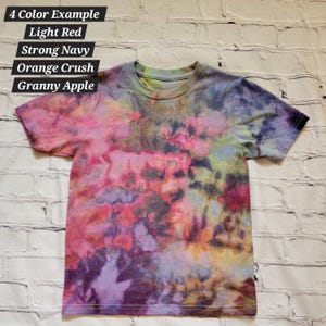 May include: A tie-dye t-shirt with a colourful abstract pattern in shades of pink, purple, blue, orange, and yellow. The shirt has a crew neck and short sleeves. The text "4 Color Example Light Red Strong Navy Orange Crush Granny Apple" is written above the shirt.