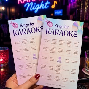 May include: Two Bingo cards for Karaoke Night, featuring song titles like "Piano Man" and "Sweet Caroline." The cards are held in a person's hand, with a neon "Karaoke Night" sign in the background.