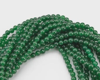 May include: Strands of glossy, deep green beads. The beads are small, round, and evenly sized, creating a smooth, flowing texture. The beads are likely used for jewelry making, such as necklaces or bracelets.