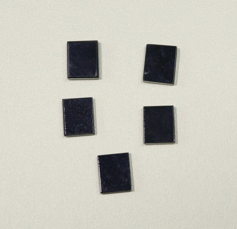 May include: Five small, square, dark blue gemstones are arranged on a light background. Each stone has a polished, reflective surface, and they are slightly different in orientation. The gemstones appear to be of uniform size and shape.