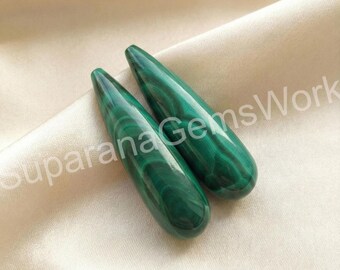 May include: Two polished malachite gemstone pendants. The teardrop-shaped stones display a rich, dark green color with swirling patterns. The pendants are displayed on a cream-colored satin fabric.