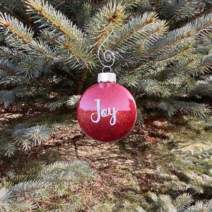 May include: Red glitter Christmas ornament with the word "Joy" in white lettering.