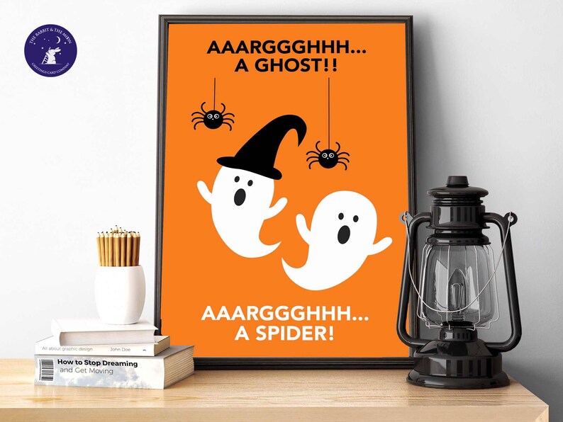 Puede incluir: Un estampado enmarcado con tem&aacute;tica de Halloween con fondo naranja. El estampado presenta dos fantasmas blancos de dibujos animados, ara&ntilde;as negras y las frases "AAARGGGHHH... A GHOST!!" y "AAARGGGHHH... A SPIDER!" en texto negro.