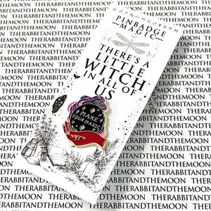 May include: A metal enamel pin featuring a red hand holding a purple and black crystal ball with the text 'MAKE YOUR MAGIC'. The pin is attached to a white backing card printed with the text 'THERE'S A LITTLE WITCH IN ALL OF US' and illustrations.