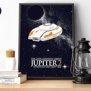 Peut inclure: Une affiche encadrée représentant un vaisseau spatial Jupiter 2 blanc et orange sur un fond d'espace étoilé bleu foncé. Le texte indique THE 24TH COLONIST GROUP JUPITER 2 INTERSTELLAR SPACE CRAFT 2046 en lettres blanches et orange.