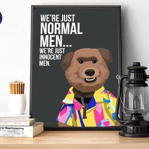 Puede incluir: Una impresión artística enmarcada con un oso de dibujos animados que lleva una camisa colorida. El texto en la impresión dice "WE'RE JUST NORMAL MEN... WE'RE JUST INNOCENT MEN." Una linterna negra y libros están sobre una superficie de madera.