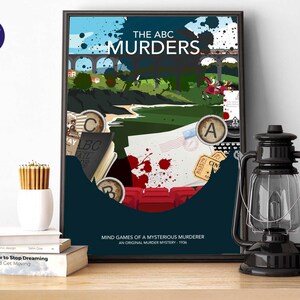 以下が含まれることがあります： 「THE ABC MURDERS」というタイトルのフレーム入りポスターと「MIND GAMES OF A MYSTERIOUS MURDERER」というテキスト。アートワークは橋、列車、文字A、B、Cを特徴としています。黒いランタンと白い鉛筆立てが木製の表面にあります。
