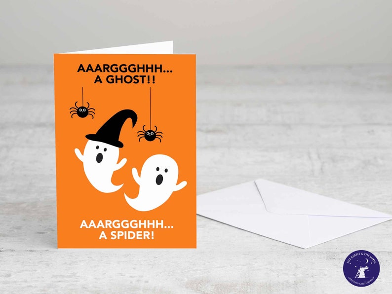 Puede incluir: Tarjeta de felicitaci&oacute;n de Halloween con fondo naranja. La tarjeta presenta dos fantasmas de dibujos animados blancos, uno con un sombrero de bruja negro y dos ara&ntilde;as negras. El texto dice "AAARGGGHHH... A GHOST!!" y "AAARGGGHHH... A SPIDER!". Se incluye un sobre blanco.