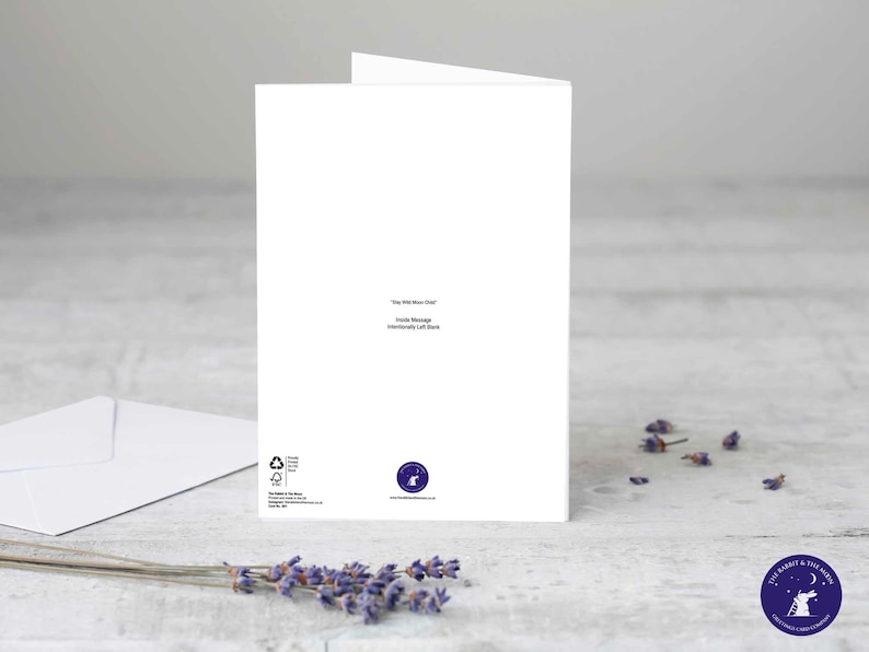 Puede incluir: Una tarjeta de felicitaci&oacute;n blanca con el texto "The Wild Moon Child" y "Inside Message Intentionally Left Blank". Tambi&eacute;n hay un sobre blanco y ramitas de lavanda. La tarjeta tiene un logotipo en la esquina inferior derecha.