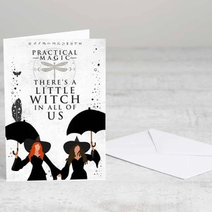 May include: A white card with a black and white illustration of two witches under umbrellas. The text on the card reads "Practical Magic" and "There's a little witch in all of us."